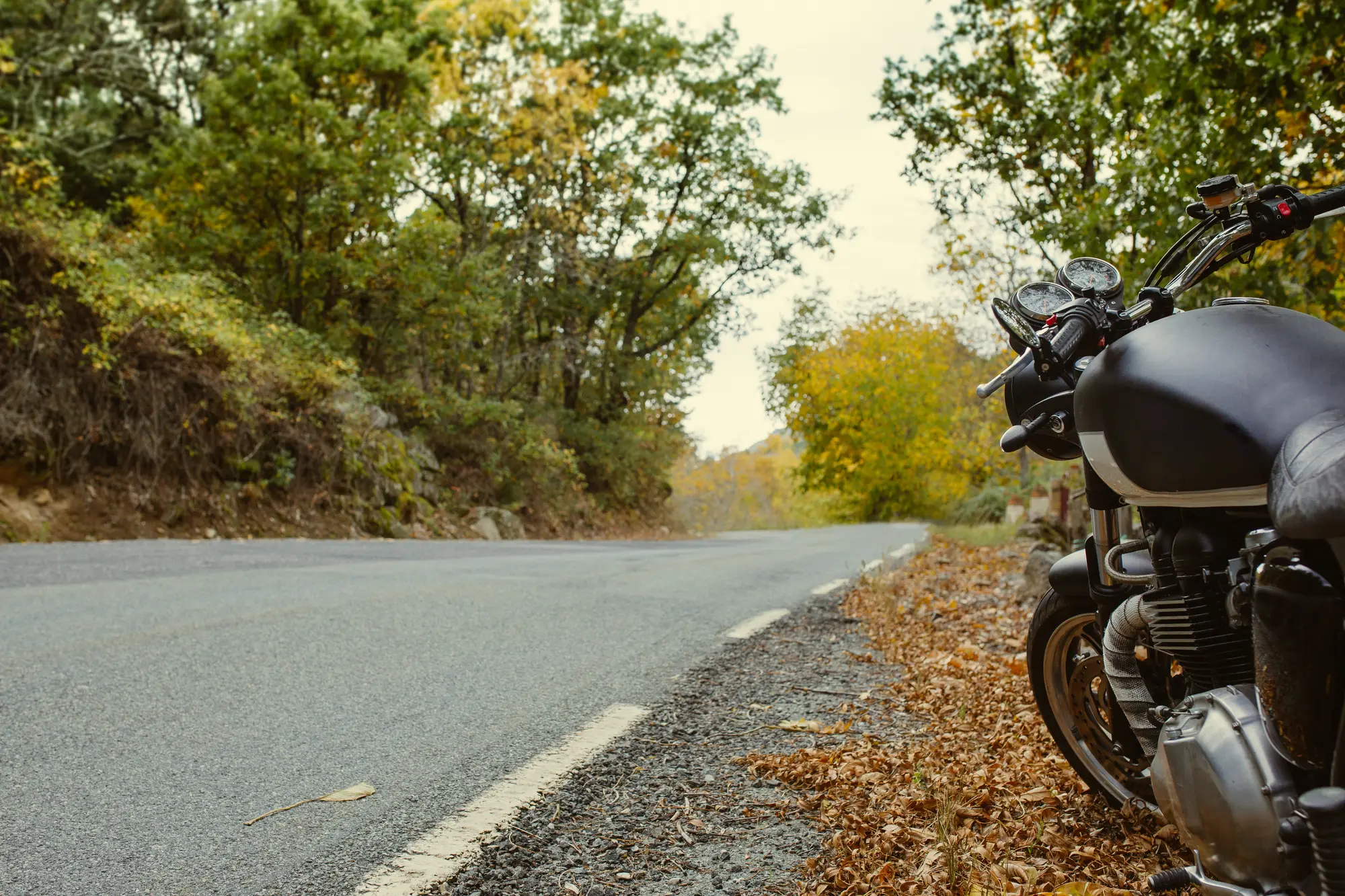 A motorcycle parked at the edge of a quiet country road in autumn