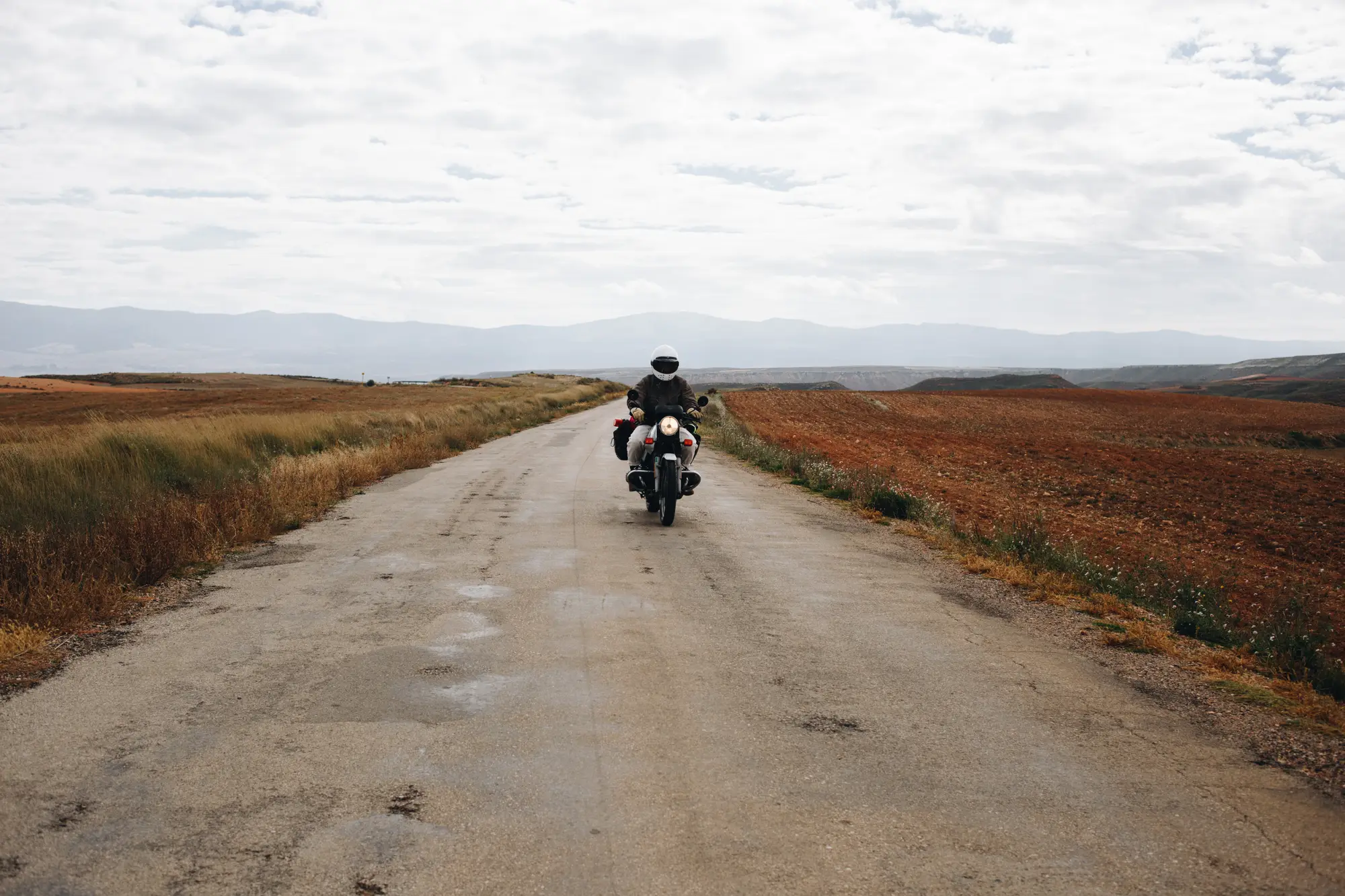 A motorcyclist riding towards the camera along a long, straight rural road